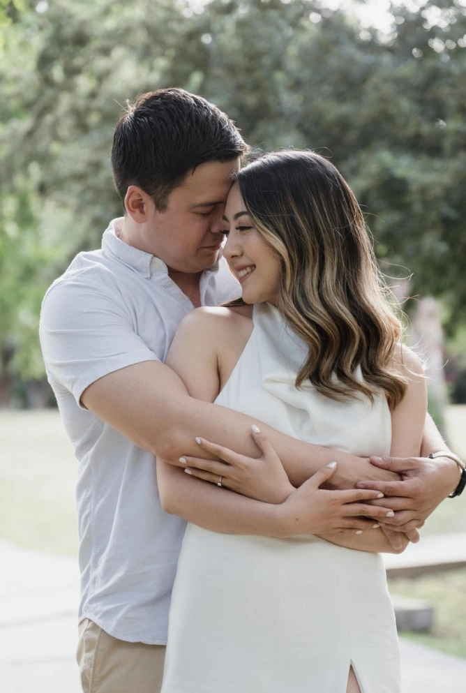Pareja abrazada en un parque, compartiendo una sonrisa íntima antes del gran día.