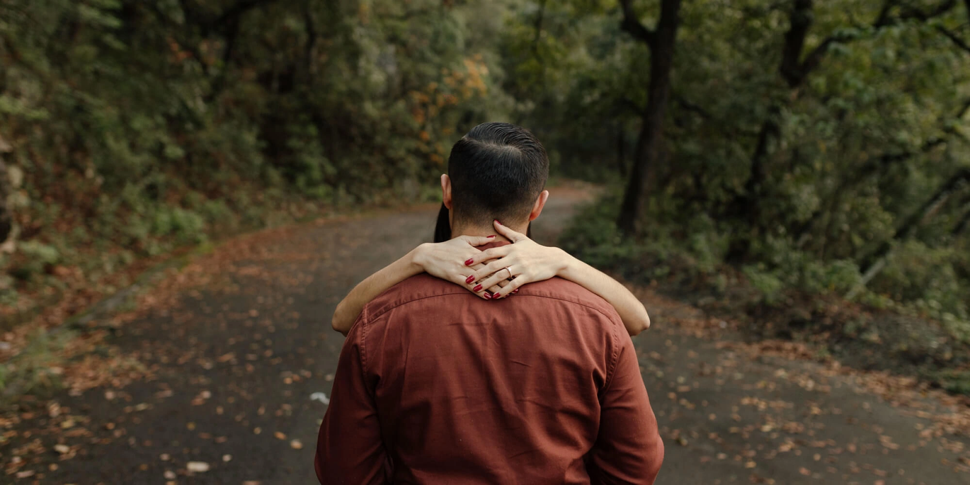 Pareja de novios caminando por un sendero en el bosque durante su sesión de fotos.