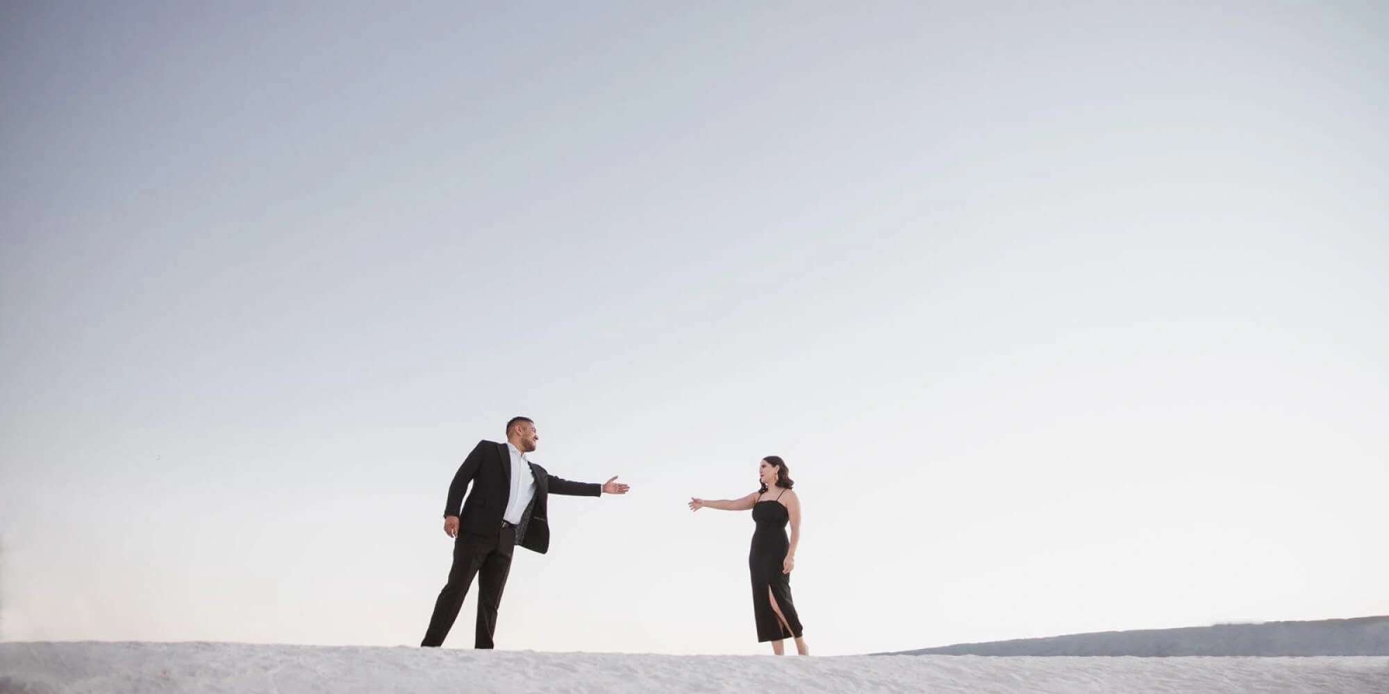 Sesión de fotos de preboda de una pareja con vestimenta elegante en un desierto de arena blanca.