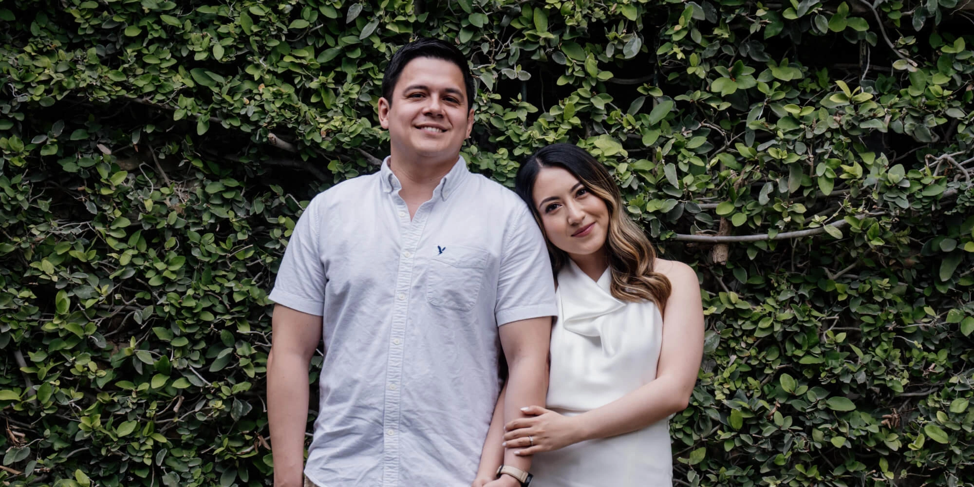 Pareja tomados de la mano y sonriendo, ideal para una sesión de fotos de preboda en un jardín urbano.