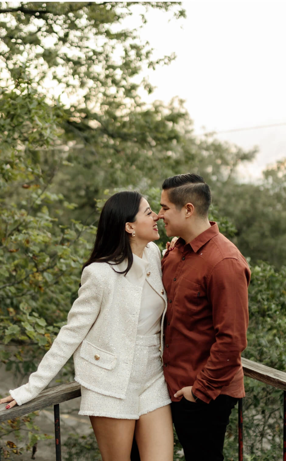 Pareja sonriendo con ternura mientras se miran frente a un paisaje natural, reflejando amor y conexión.